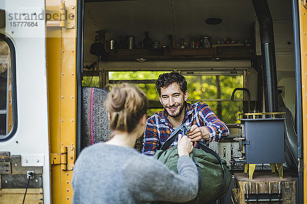 Lächelnder Mann gibt der Frau Gepäck zum Ausladen aus dem Wohnwagen beim Camping