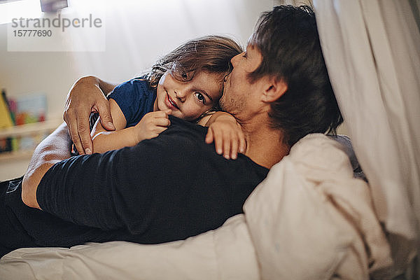 Porträt eines lächelnden Mädchens mit reifem Vater auf dem Bett liegend