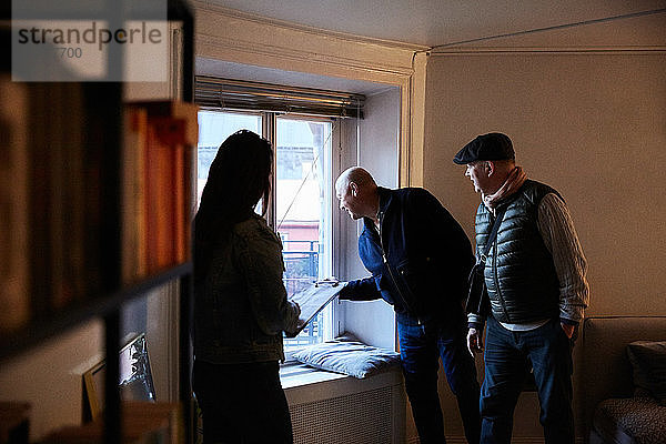 Ältere Männer schauen durch das Fenster  während sie mit der Besitzerin zu Hause stehen