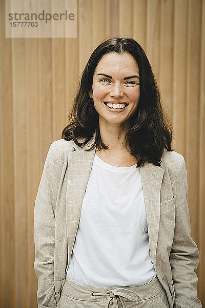 Porträt einer glücklichen Unternehmerin  die an einer Holzwand steht