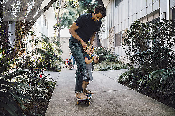 Glücklicher Vater und Tochter beim Skateboarden auf dem Fussweg