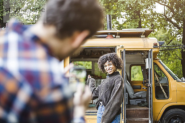 Fröhliche junge Frau posiert beim Zelten für ihren Freund gegen ein Wohnmobil