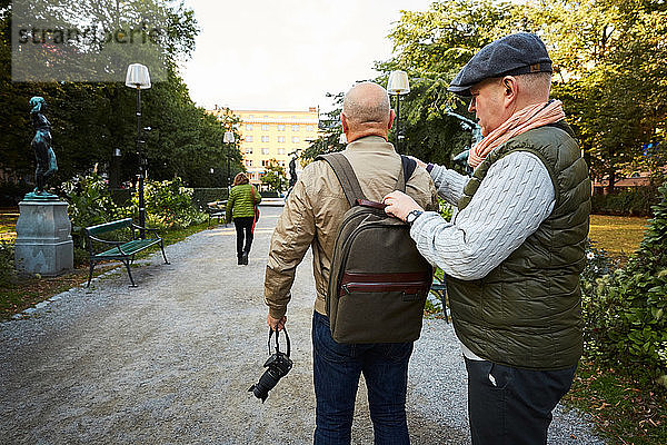 Älterer Mann verstellt den Taschengurt eines Freundes  während er im Park in der Stadt steht
