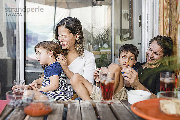 Glückliche Eltern sitzen mit Kindern am Tisch gegen eine Glastür