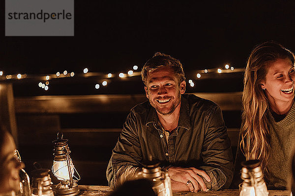 Lächelnder Mann sitzt abends mit Freundin im Restaurant