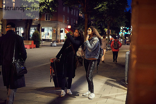 Lesbisches Paar in voller Länge mit Gepäck steht nachts in der Stadt auf dem Bürgersteig