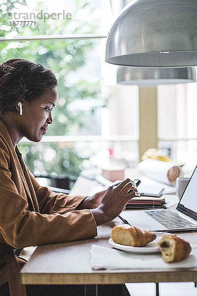 Selbstbewusste Unternehmerin telefoniert  während sie zu Hause am Tisch sitzt
