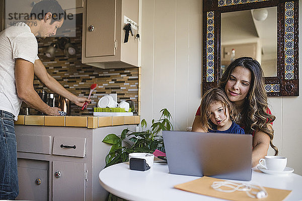 Mutter und Tochter benutzen Laptop  während der Vater in der Küche arbeitet