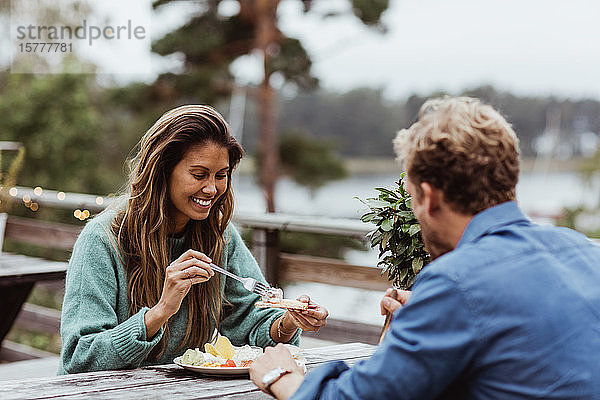 Lächelnde Frau isst Essen  während sie mit einem männlichen Freund im Restaurant sitzt