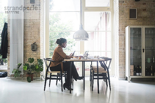 Architektin telefoniert  während sie zu Hause am Tisch sitzt