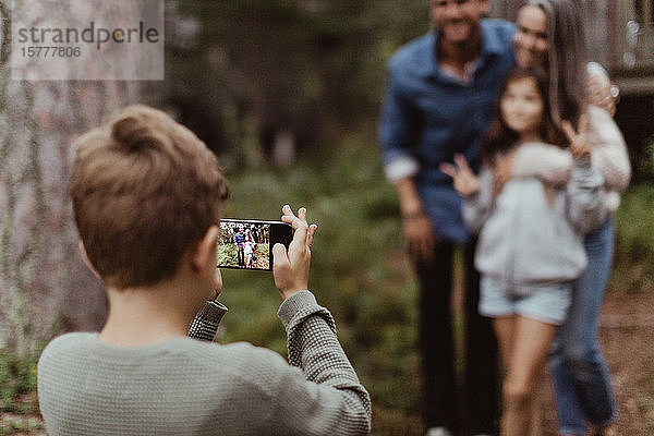 Junge fotografiert Familie mit Mobiltelefon  während er im Hinterhof steht