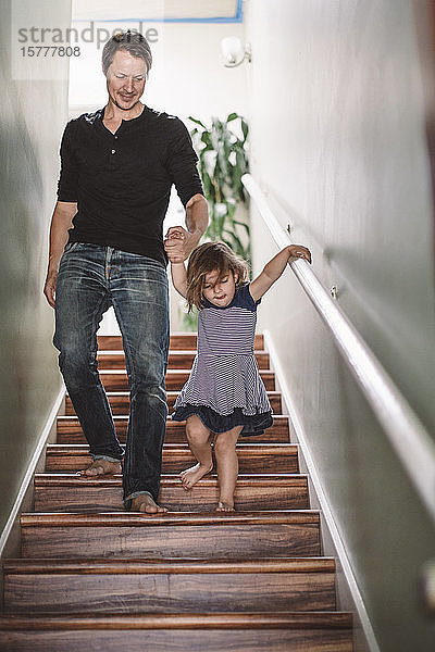 Lächelnder Vater hält der Tochter beim Treppensteigen zu Hause die Hand
