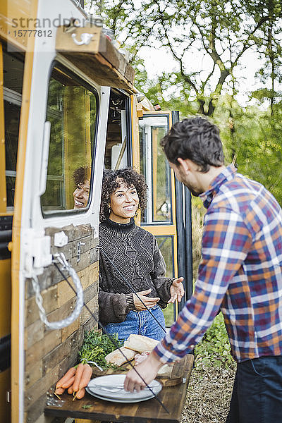 Lächelnde junge Frau unterhält sich während der Essenszubereitung beim Camping mit ihrem Freund