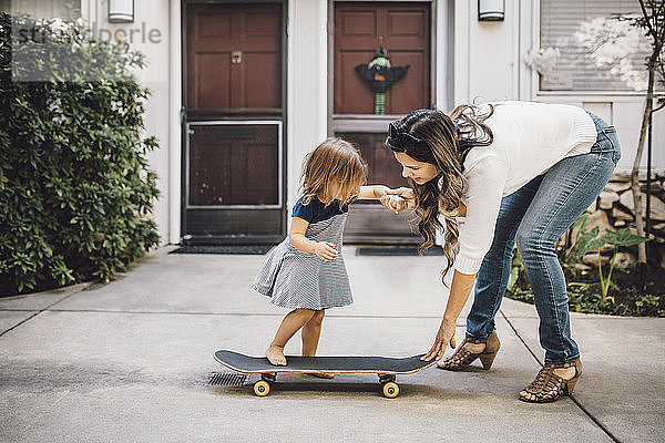 Skateboardfahren der Tochter mit Hilfe der lächelnden Mutter auf dem Fußweg