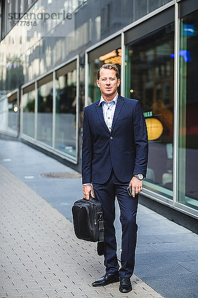 Porträt eines reifen Geschäftsmannes mit Tasche vor Bürogebäude stehend