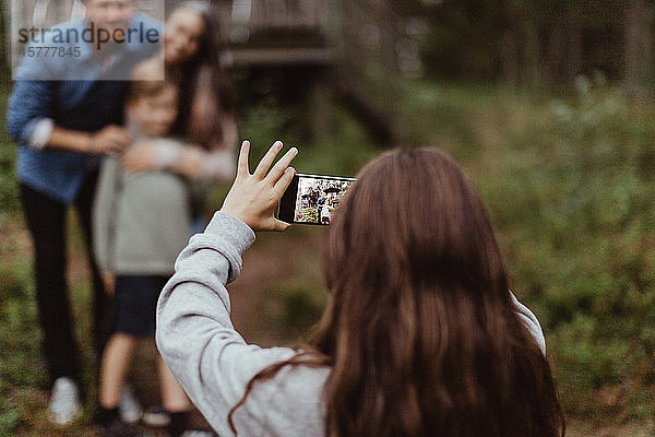 Mädchen fotografiert Familie mit Mobiltelefon  während sie im Hinterhof steht