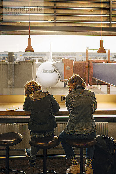 Rückansicht von Bruder und Schwester  die am Flughafen vor dem Fenster sitzen