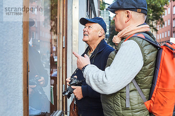 Älteres schwules Ehepaar steht während des Urlaubs in der Stadt am Schaufenster mit Kamera