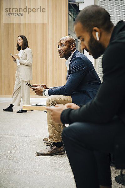 Männliche und weibliche Berufstätige schauen weg  während sie ein Smartphone außerhalb des Büros in der Hand halten