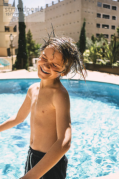 Lächelnder Junge ohne Hemd  der sich am Swimmingpool des Ferienorts vergnügt