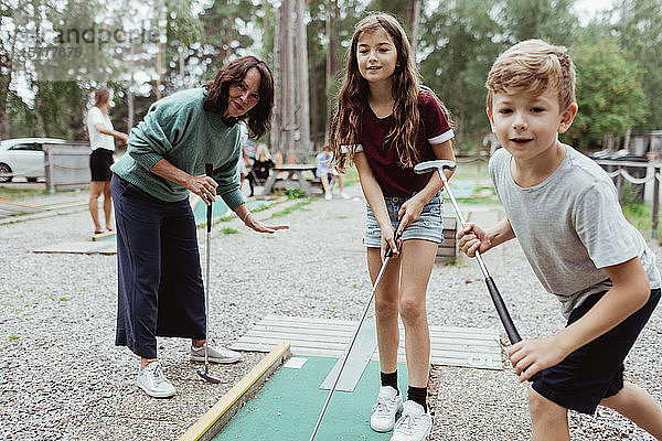 Geschwister spielen im Urlaub mit der Familie im Garten Minigolf