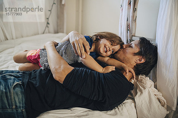 Reifer Vater küsst Tochter im Bett liegend