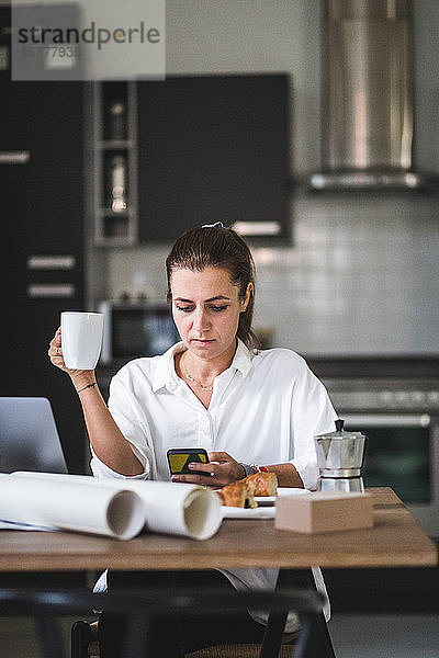 Weibliche Freiberuflerin telefoniert  während sie mit Kaffeetasse zu Hause sitzt