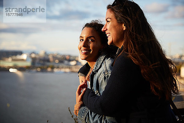 Lächelndes lesbisches Paar steht am Fluss in der Stadt gegen den Himmel