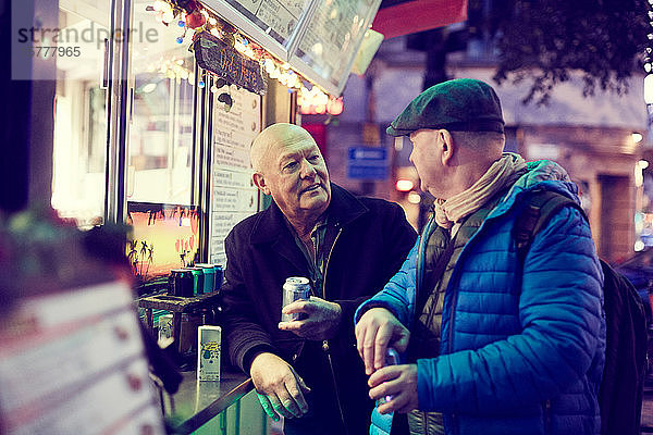 Älteres schwules Ehepaar stellt sich nachts in der Stadt gegen einen Kiosk