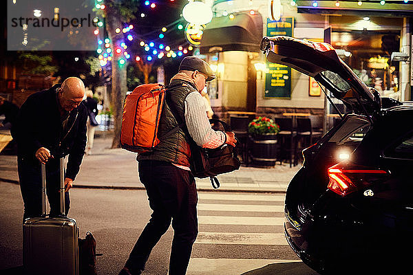 Homosexuelles Paar  das nachts in der Stadt Gepäck im Kofferraum eines Autos auf die Straße stellt