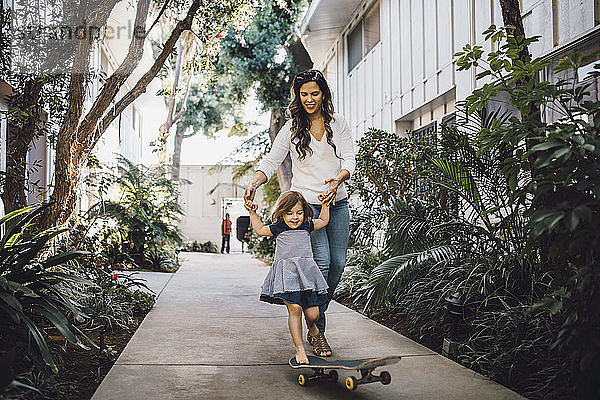 Lächelnde Tochter beim Skateboarden mit Hilfe der Mutter auf dem Fußweg