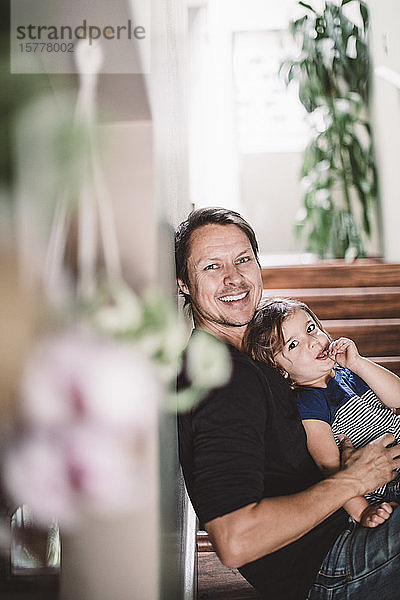 Porträt eines glücklichen Vaters mit Tochter  der zu Hause auf Stufen sitzt