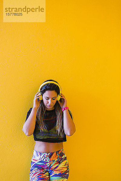 Frau mit Kopfhörern an gelber Wand