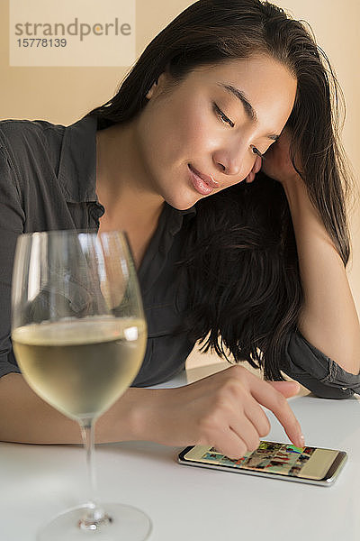 Frau benutzt Smartphone neben einem Glas Wein