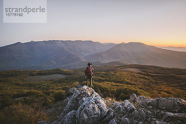 Mann auf einem Felsen in den Bergen bei Sonnenuntergang