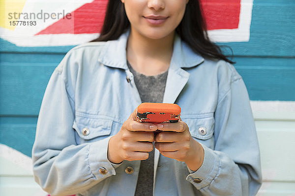 Lächelnde Frau hält Smartphone gegen bunte Wand