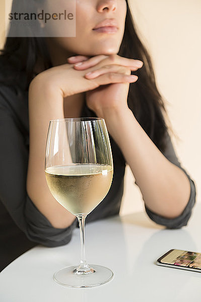 Frau am Tisch mit Smartphone und einem Glas Wein