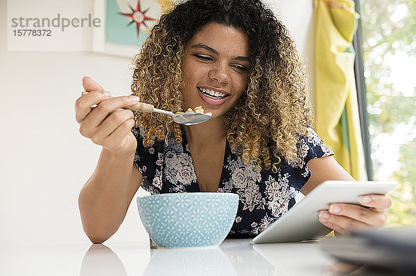 Lächelnde Frau  die ein Tablet benutzt  während sie frühstückt
