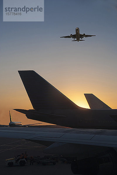 Flugzeug fliegt über Flugzeug auf Landebahn bei Sonnenuntergang