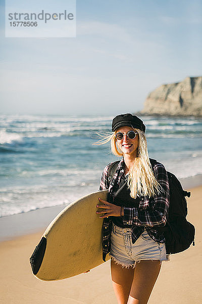 Lächelnde Frau mit Surfbrett am Strand
