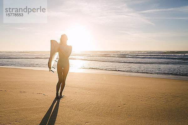 Frau hält Surfbrett gegen das Sonnenlicht am Strand