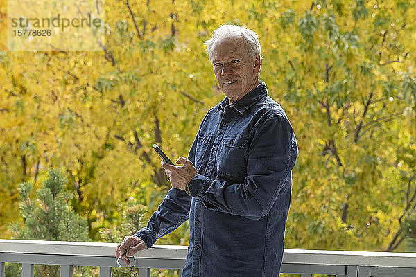 Lächelnder Mann mit Telefon in der Hand zwischen Herbstbäumen