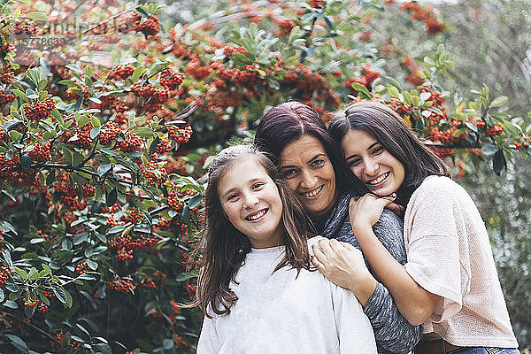 Mutter und Töchter lächelnd und sich umarmend am Busch