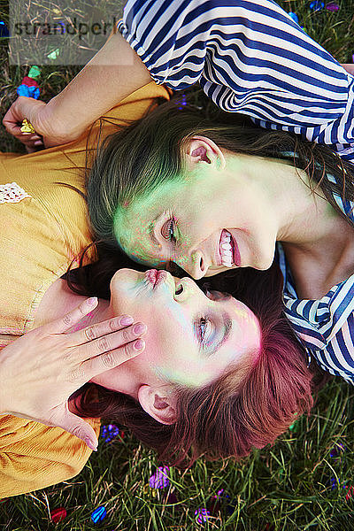Zwei mit farbigem Kreidepulver bedeckte junge Frauen liegen auf Gras beim Holi-Fest  Draufsicht