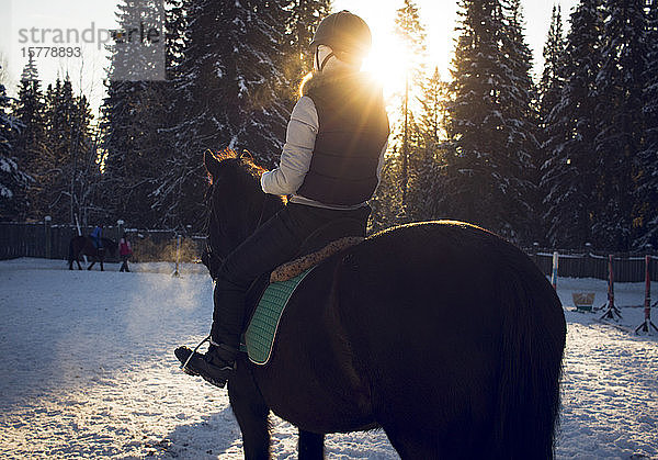 Mädchen reitet Pferd bei Sonnenuntergang