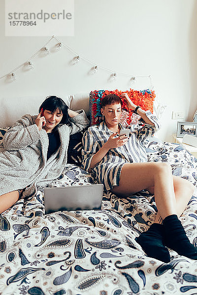 Frauen entspannen sich am Bett mit Laptop und Mobiltelefon