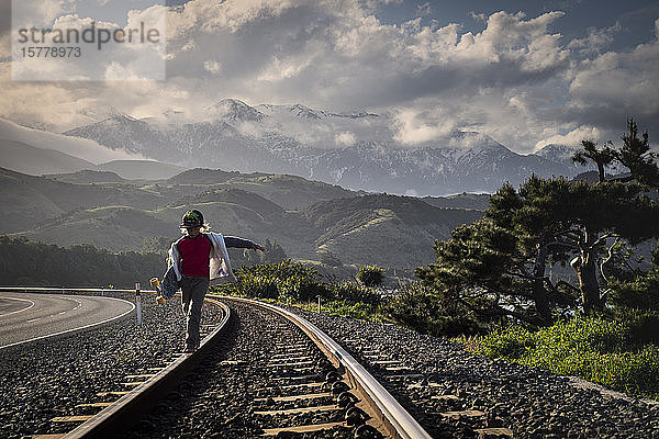 Junge  der entlang einer Eisenbahnlinie geht und ein Skateboard hält  Kaikoura  Gisborne  Neuseeland