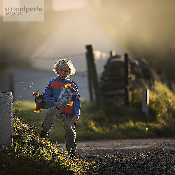 Porträt eines Jungen in ländlicher Umgebung  der ein Skateboard hält  Lahinch  Clare  Irland