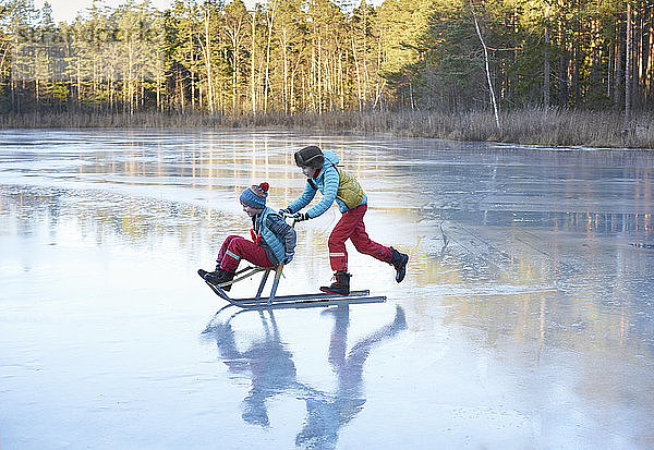 Junge schiebt seinen Bruder im Schlitten über den gefrorenen See