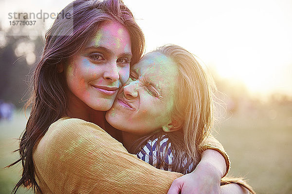 Zwei junge Frauen mit mit farbigem Kreidepulver bedeckten Gesichtern umarmen sich beim Holi-Fest  Porträt